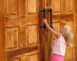 Young child attempting to open large wood doors